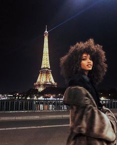 a woman with an afro standing in front of the eiffel tower at night