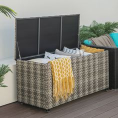 an outdoor storage bench with cushions and blankets on the floor next to potted plants