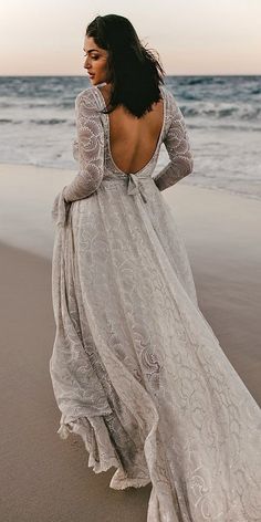 a woman standing on top of a beach next to the ocean wearing a white dress