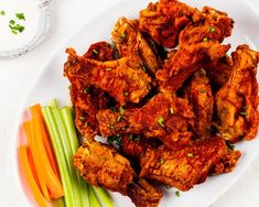 chicken wings with celery and carrots on a white plate next to a napkin