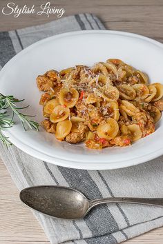 a white plate topped with pasta and meat covered in sauce on top of a wooden table