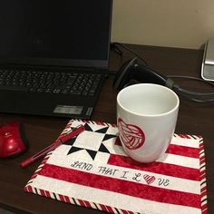 a coffee cup sitting on top of a red and white place mat next to a laptop