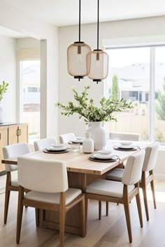 a dining room table with white chairs and a vase filled with flowers on top of it