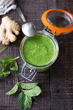 a glass jar filled with green liquid next to some leaves and a spoon on a wooden table