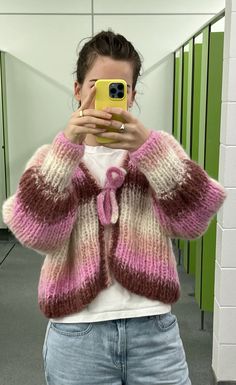 a woman taking a selfie in front of a mirror wearing a pink and white cardigan