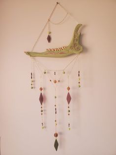 a green bird hanging from the side of a wall with beaded necklaces attached to it