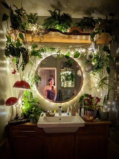 a bathroom with plants growing on the wall and a mirror above it that is lit up