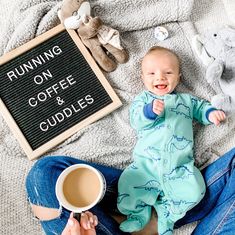 a baby sitting on the floor next to a cup of coffee and stuffed animals with a sign that says running on coffee cuddles