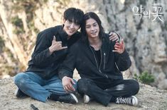 two young men sitting on top of a rocky hill giving the peace sign with their hands