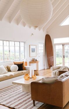 a living room filled with furniture and a surfboard hanging from the ceiling in front of two windows