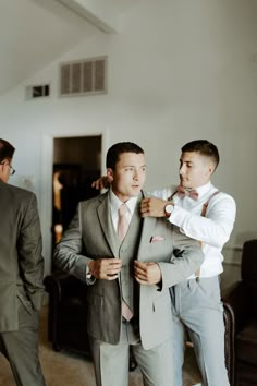 two men in suits are fixing their ties