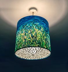 a blue and green lamp shade hanging from the ceiling in a room with dark walls