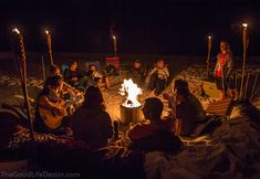 a group of people sitting around a campfire with torches in the sand at night