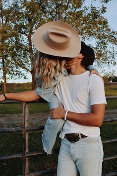 a young man and woman embracing in front of a fence