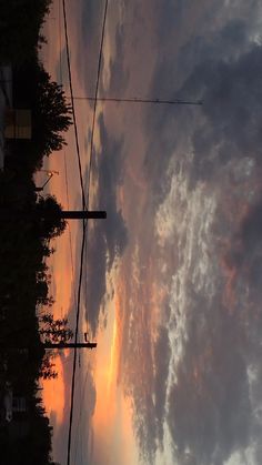 the sky is filled with clouds as the sun sets in the distance behind some power lines