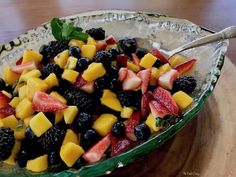 a glass bowl filled with fruit salad on top of a wooden table