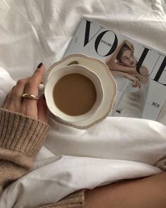 a woman laying in bed holding a cup of coffee next to a magazine with the word voie on it