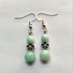 two green beads are hanging from silver earwires on a white tablecloth with a pair of earrings in the foreground