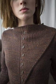 a woman wearing a brown sweater with buttons on the front and back, standing in front of a window