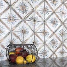 a wire basket filled with fruit sitting on top of a counter next to a tiled wall