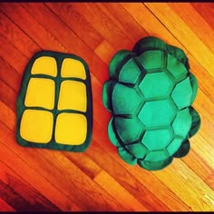 two cakes made to look like turtles on a wooden floor, one is green and the other is yellow