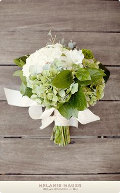 a bouquet of white and green flowers on top of a wooden table next to a wall