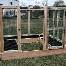 an outdoor chicken coop made out of wood and wire with the door open to let birds inside