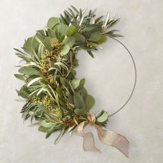 a wreath with greenery and gold ribbon hanging on a wall