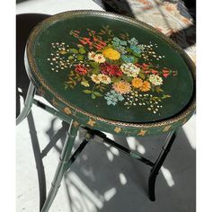 an old green table with flowers painted on the top and bottom, sitting next to a chair