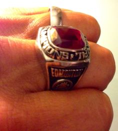 a close up of a person's hand holding a ring with a red stone