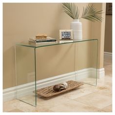 a glass console table with a basket on the floor next to it and a potted plant