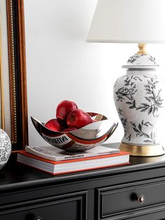 a white vase sitting on top of a table next to a bowl filled with apples