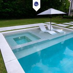 an empty swimming pool with lounge chairs and an umbrella in the grass next to it