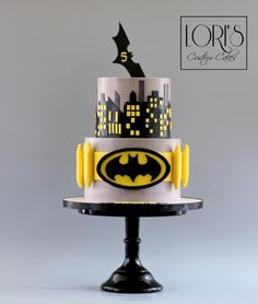 a three tiered cake decorated with batman symbol and cityscape on the top