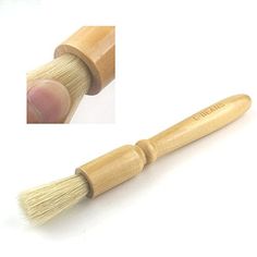 a hand holding a small wooden brush on top of a white surface