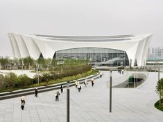 people are walking around in front of a large building with a curved roof and glass windows