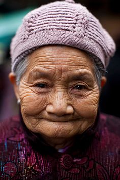 an old woman with wrinkles and a hat on her head, looking at the camera