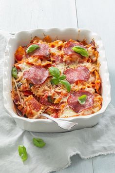 a casserole dish with pepperoni, cheese and spinach on a white cloth