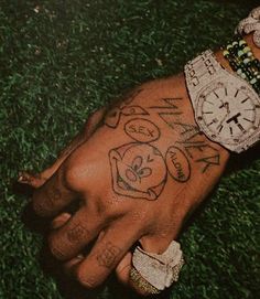 a person with tattoos on their arm and wrist is holding onto a watch in the grass