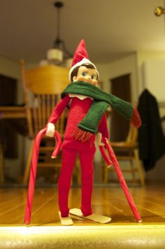 an elf with a green scarf and red pants is standing on a wooden floor in front of a chair