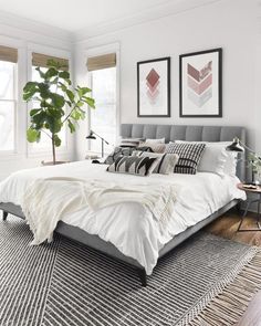 a bed with white sheets and pillows in a bedroom next to two plants on the floor