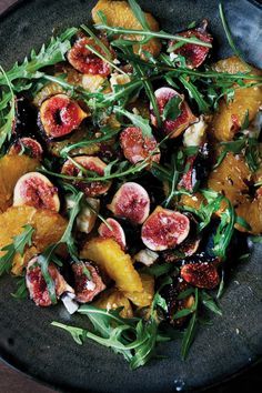 a black plate topped with fruit and greens