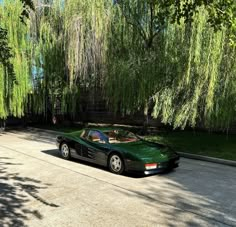 a green sports car parked on the side of a road next to a willow tree