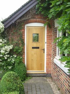 a house with a wooden door and brick walkway leading to the front door is surrounded by greenery