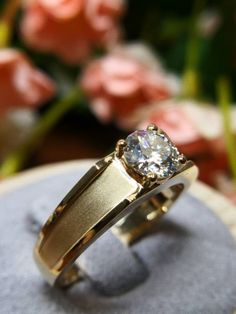 a close up of a ring on a rock with flowers in the backgroud