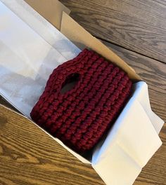 a red knitted object sitting inside of a white box on top of a wooden table