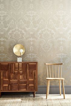 a wooden chair sitting next to a dresser in front of a wallpapered wall