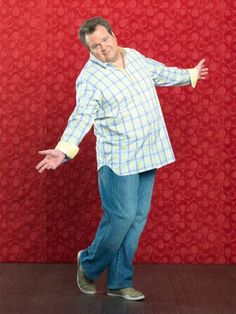 a man standing in front of a red wall with his arms out and hands outstretched