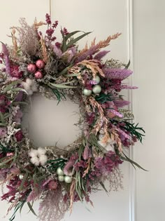 a wreath hanging on the front door with purple flowers and greenery around it's edges