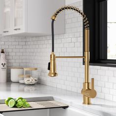 a kitchen sink with gold faucet and green vegetables on the counter next to it